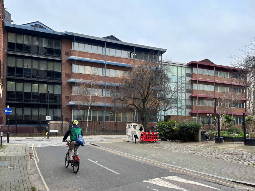 A cyclist rides past a three-story office building with large windows on a quiet street with some trees.