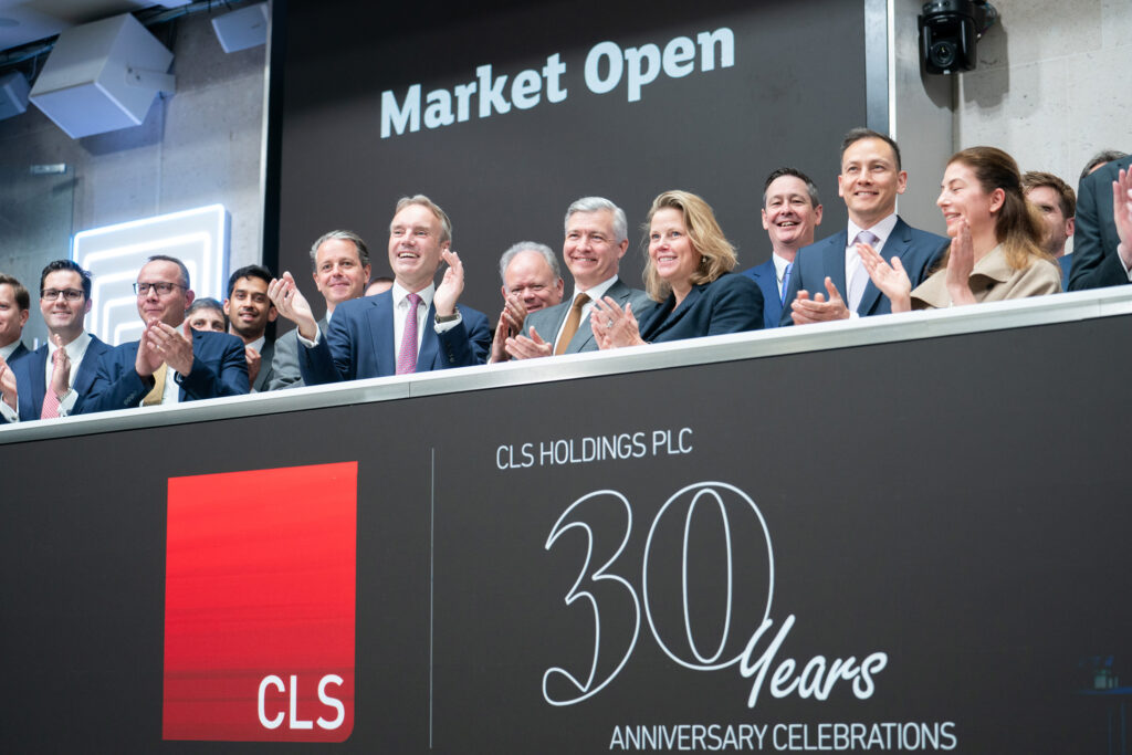 A group of business people in suits clapping at a podium under a sign reading "Market Open." A screen displays "CLS Holdings PLC 30 Years Anniversary Celebrations.