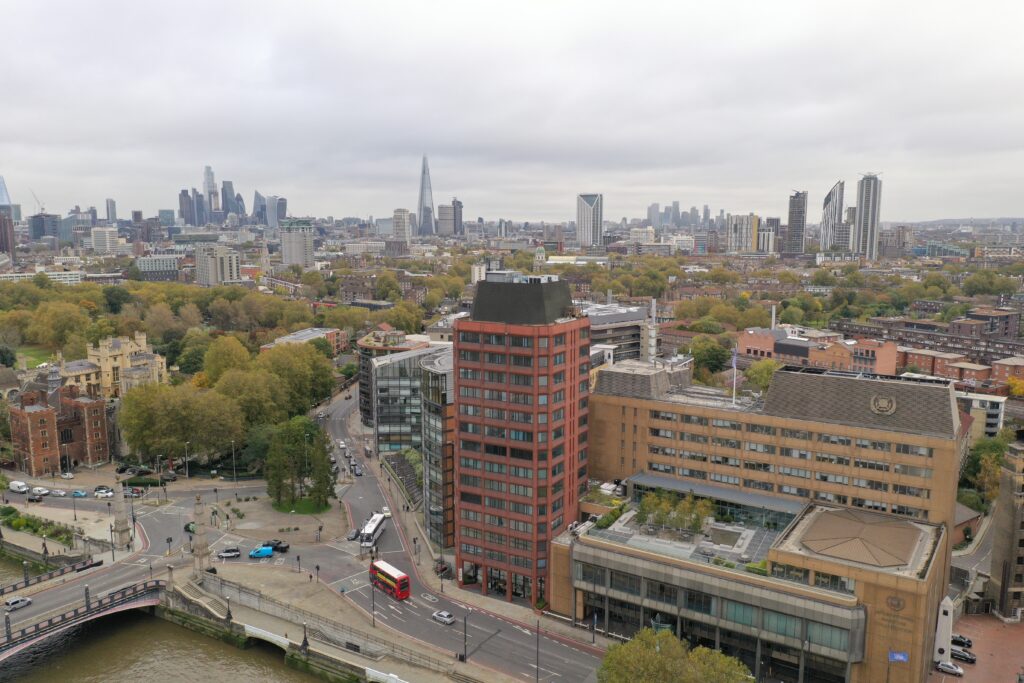 Aerial view of a cityscape featuring a mix of modern and traditional buildings, with a red brick building in the foreground and the Shard visible in the background.