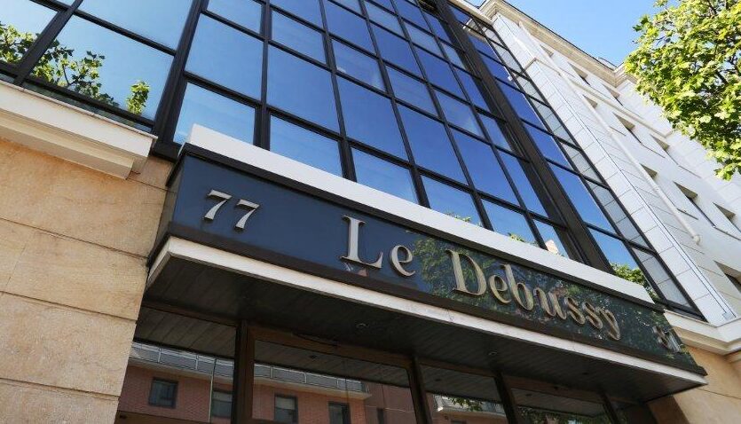 Exterior of a modern building with large reflective windows and the sign "77 Le Divinys" above the entrance.